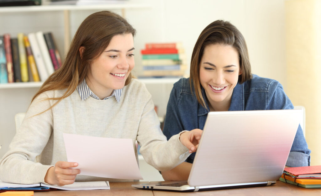 Two students learning together on line comparing notes with a laptop at home